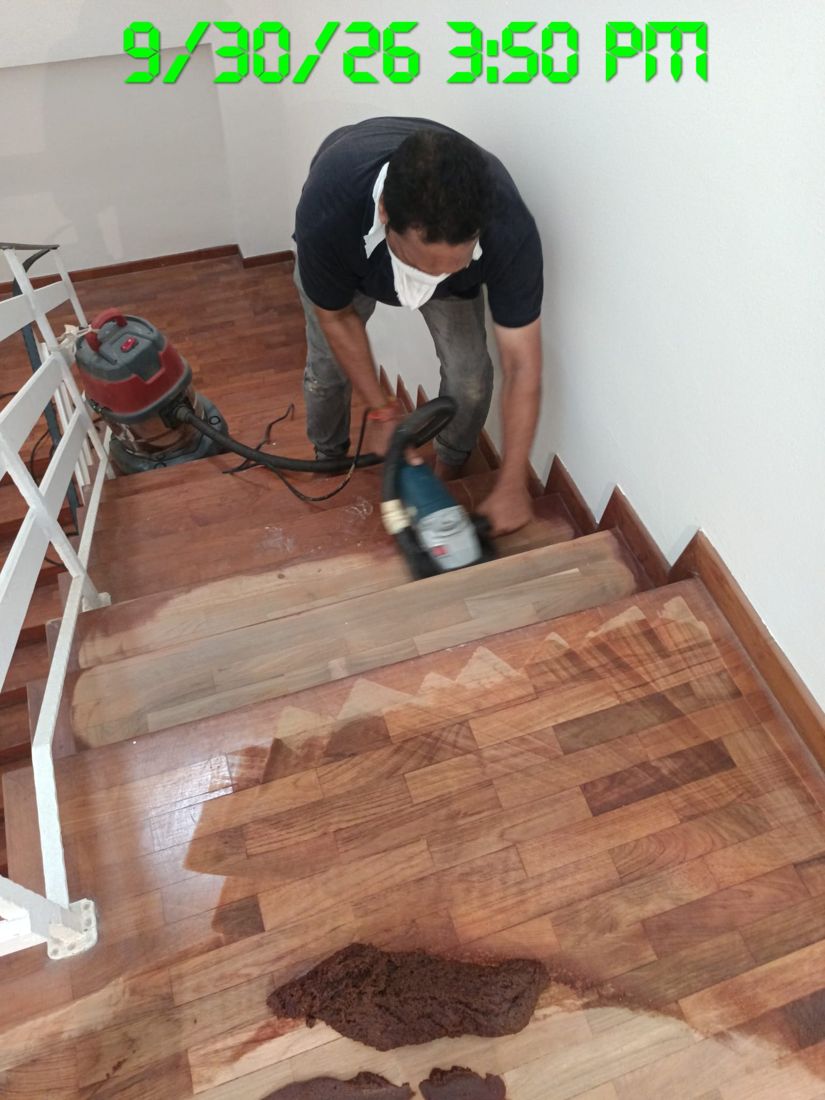 Technician sanding old varnish off a timber staircase landing, half done